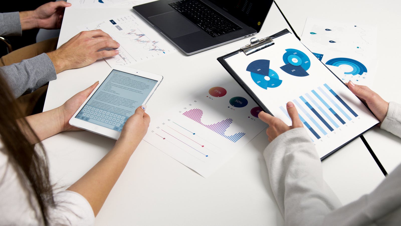 Photo by Artem Podrez Team analyzing financial charts and digital reports during a business meeting.