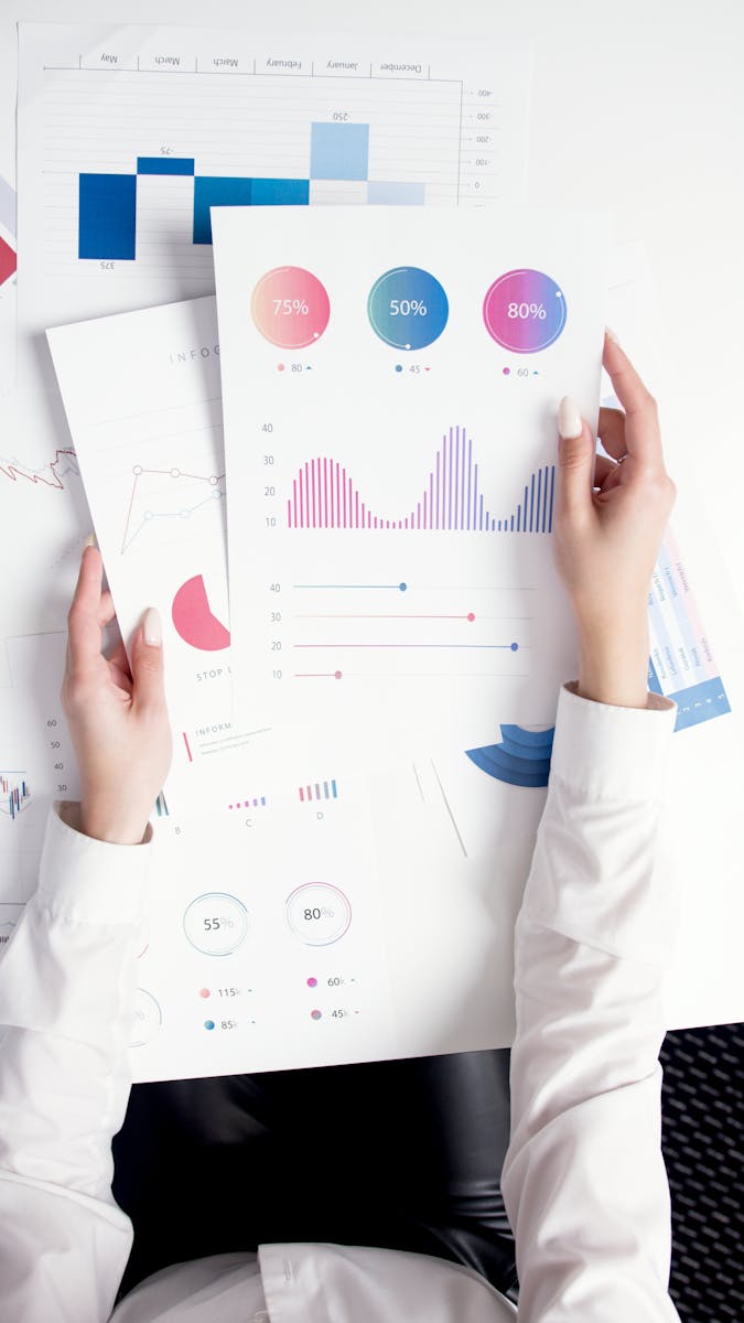 Photo by Artem Podrez Close-up of hands analyzing colorful business data reports in an office setting.
