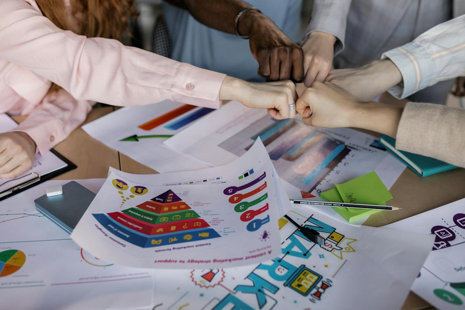 Photo by Alena Darmel A diverse team unites hands over business reports and marketing strategies, symbolizing teamwork.