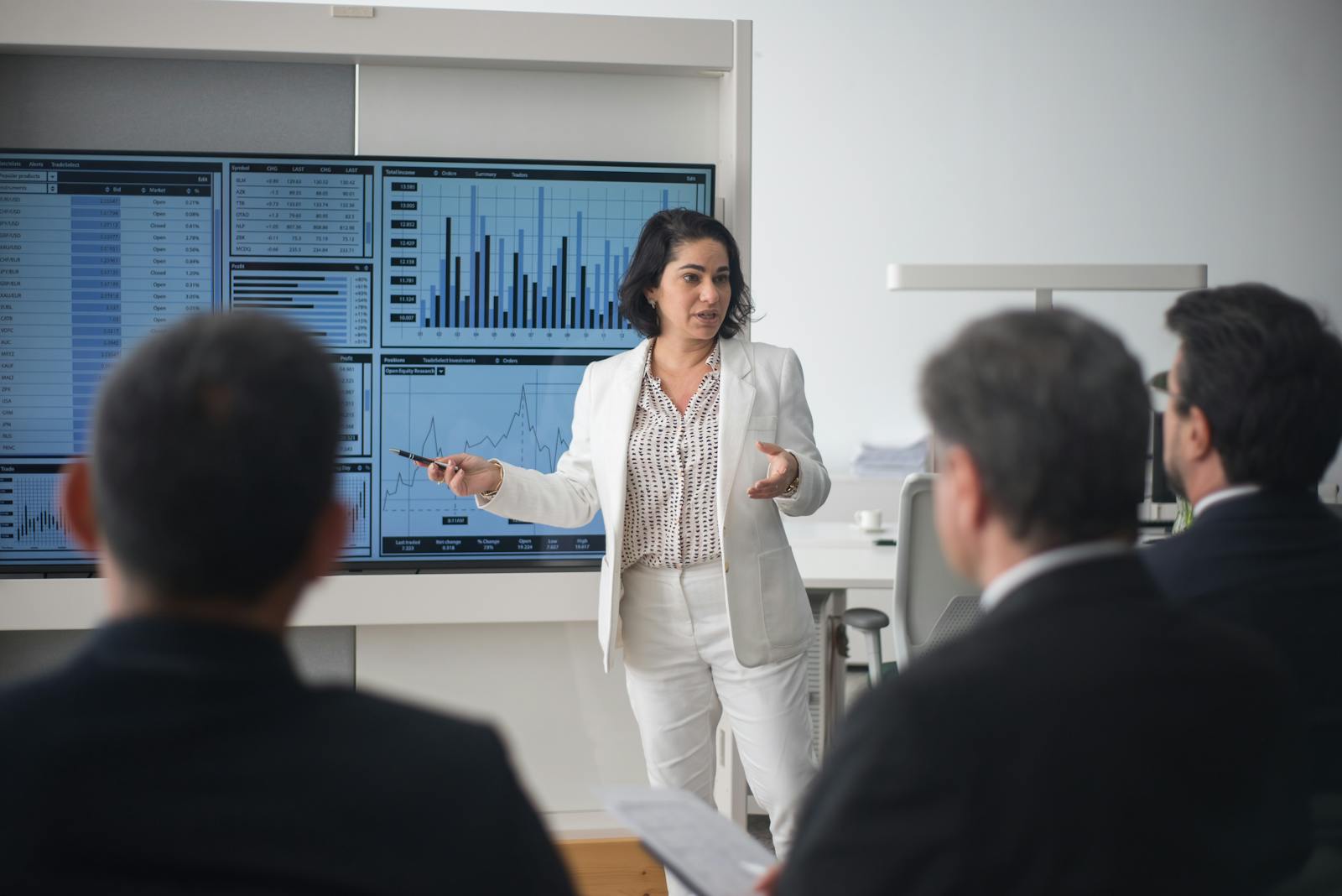 Photo by Kampus Production Professional woman presenting stock market data in a modern office setting.