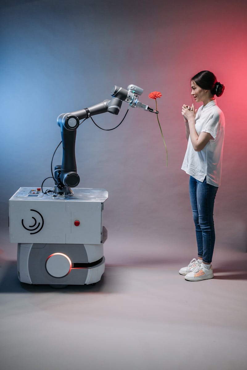 Photo by Pavel Danilyuk A robot arm presents a flower to a smiling woman, illustrating human-robot interaction.