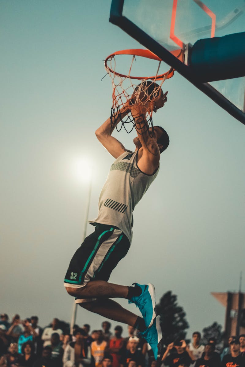 Photo by Wallace Chuck Athlete performs a powerful dunk on an outdoor basketball court at dusk.