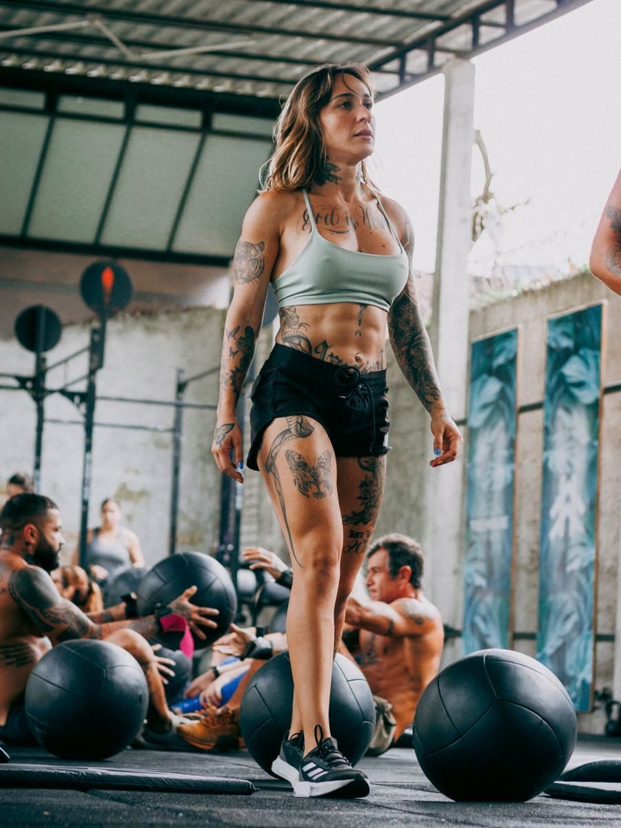 Tattooed woman leading a CrossFit class outdoors, emphasizing fitness and motivation.